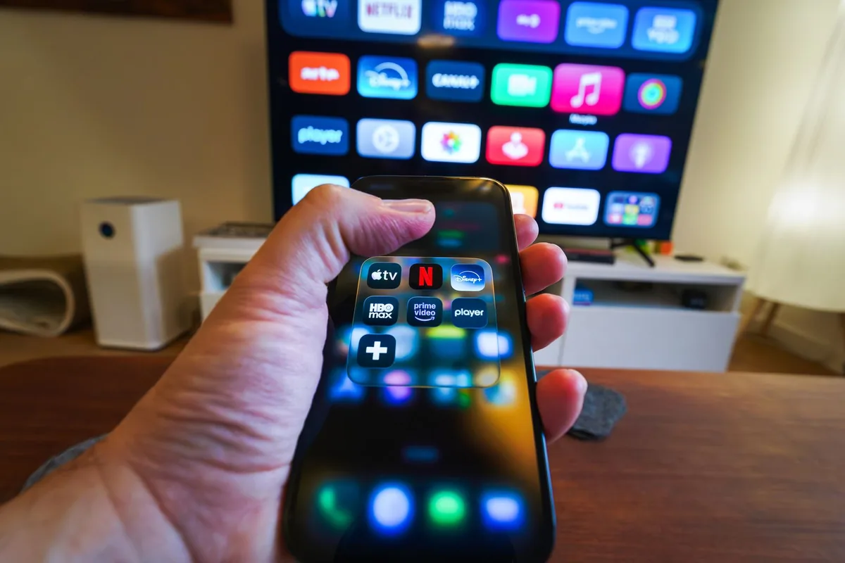 テレビの前で、動画配信アプリのアイコンが並んだスマホを持つ手