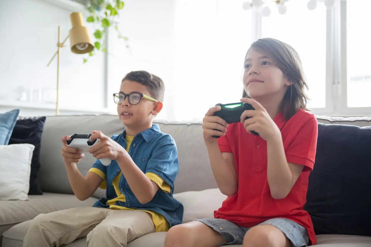 ソファに並んで座り、コントローラーを持って一緒にゲームをしている2人の子ども